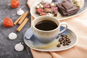 A cup of coffee with chocolate and coconut candies on a black concrete background and orange textile