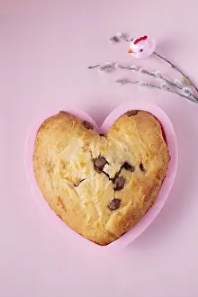 Cupcake in the shape of a heart with pieces of chocolate and willow branches on a pink background