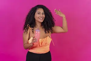 Curly-haired woman in summer clothes on a pink background drinking heated water