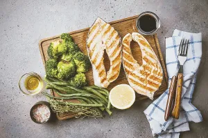 Cutting board with grilled salmon steaks and vegetables on gray table