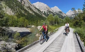 Cyclists, mountain bikers cycle on bridge over mountain stream