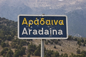 Category Mountain Landscapes Prints: Damaged road sign with Greek and Latin lettering in front of a mountain landscape