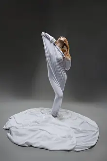 A dancer stands elegantly, skillfully emerging from cascading white fabric in a serene studio