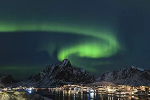 Dancing green polar lights over the village Reine on the Lofoten islands in Norway at night in winter with snow capped
