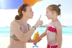 Daughter and mother in beach with sunscreen in bikini