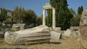 Debris of a fallen column lying on dry ground in front of a stone archway
