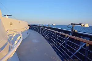 Deck of a cruise ship with clear blue sky and blue railing