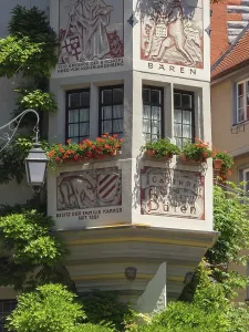 A decorated half-timbered house with murals and red geraniums in full bloom