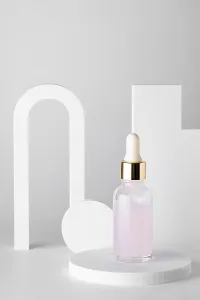 A delicate pink serum in a glass dropper bottle is elegantly displayed on white podiums against a minimalistic backdrop