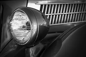 Detailed black and white close-up of a vintage car's headlight and grille in St
