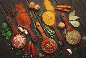 Different types of spices are arranged in wooden spoons on a dark table