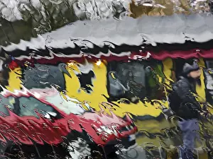 Distorted view through a rain-soaked car window pane onto a car and a house