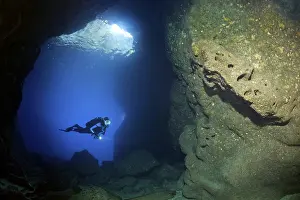Diver with lamp in rocky cave, sparse growth