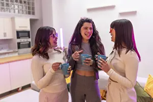 Three diverse young women laughing and talking while holding coffee mugs