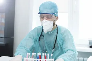 Doctor in protective gear sits at a laboratory table with test tubes