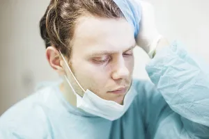 A doctor in scrubs showing concern with hand on head
