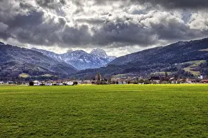 Dramatic Alpine landscape with green meadow in the foreground and cloudy sky over a village