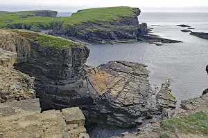Dramatic rocky coastline with green cliffs and calm sea under a cloudy sky
