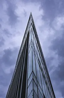 Dramatic shot of a glass skyscraper with an acute angle against a cloudy sky