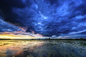 Dramatic sunset over flooded wetlands with wind turbines in the background and bright shades of orange in the sky
