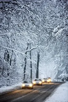 Driving in winter, vehicles on a cleared road in a snow-covered forest with falling snow