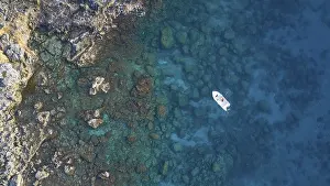 Drone shot, boat in clear blue water next to rocks and corals