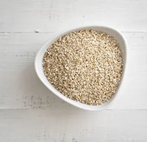 Dry barley grits in white bowl on a wooden background