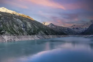 Early morning light over a lake with snow-covered mountains and pink sky