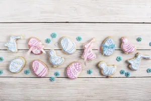 Easter frosted cookies in shape of egg chicken and rabbit on white wooden table background along with sugar sprinkles
