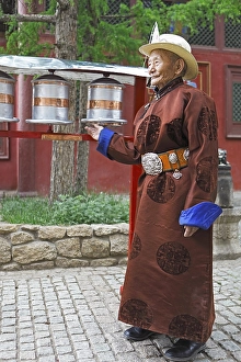 Elderly man wearing a traditional deel while rotating prayer wheels in the Buddhist Gandan Monastery, Ulaanbaatar, Mongolia, Asia