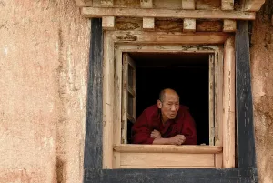 Category Buddhism Prints: Elderly Tibetan monk looking out the monastery window of the Tibetan Buddhist monastery