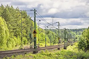 Electric railway line with overhead line in a deciduous forest in spring