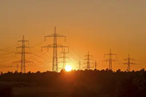 Electricity pylons in front of a glowing sunset on the horizon