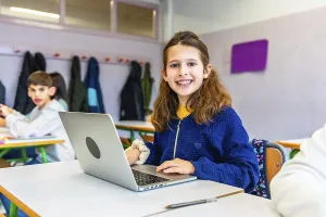 Elementary school student smiling and using laptop during class