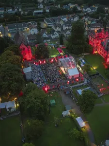 Evening aerial view of a concert with illuminated buildings and a crowd of people facing the stage