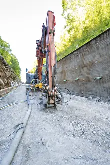 Excavator in action on a construction site next to a concrete wall with pipes