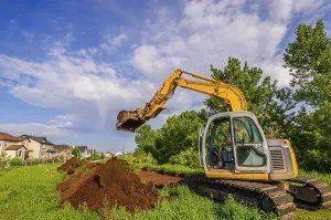 An excavator digging up soil to construct a pathway next to a row of houses