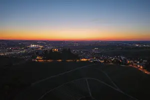 Expansive city view at dusk, with illuminated chapel and vineyards