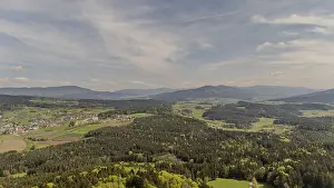 Expansive view of forest and mountains under a cloudy sky with diffuse sunlight