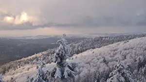 Extensive winter landscape with forests and mountains under a dramatic sky