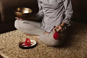 Faceless woman meditates at home on carpet and plays on copper singing bowl