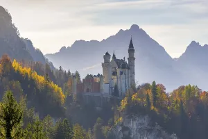 Fairytale Neuschwanstein Castle surrounded by autumnal trees against a mountain backdrop