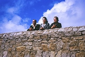 Familie blickt ueber eine Mauer gegen einen blauen bewoelkten Himmel, unbekannter Ort, Grossbritannien 1964