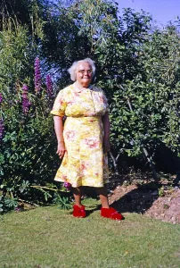 Familienportraet in voller Laenge Grossmutter in gebluemtem Kleid stehend im Garten, britische Kultur 1967 traegt rote Hausschuhe