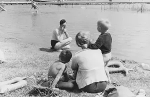 Family in the 1950s. A mother and her children sits on the beach while her husband is filming her with a amateur film camera. The film was then developed and shown on a film projector on a fold up screen. The film had no sound