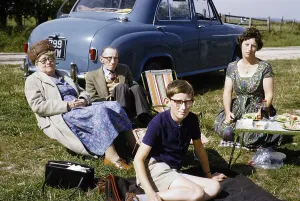 Family picnic in the countryside sitting on grass by car, South Downs, West Sussex, England photographed in 1962