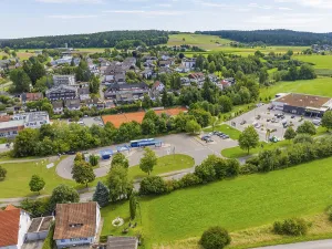 Far-reaching view of a village with green fields and a central car park under a blue sky