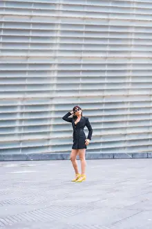 Fashion pose. Brunette girl in the city with a red bag walking around a building