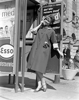 Fashionable in the 1950s. A young woman wears a typical 1950s coat. She poses in the outfit while pretending to speak on a phone in a phone box. Sweden 1950s. Photo Kristoffersson Ref 315A-7