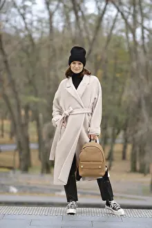 A fashionable woman stands confidently in a light coat and black beanie